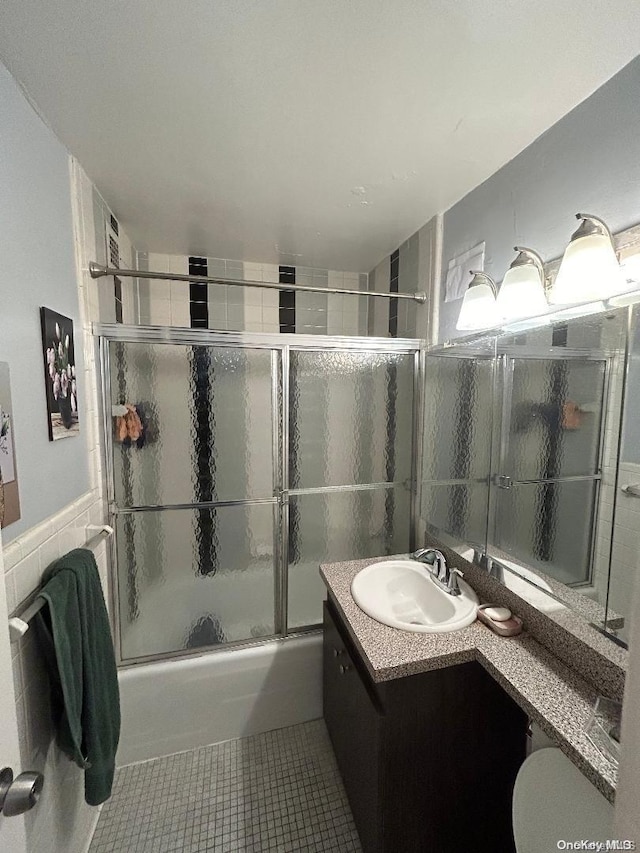 bathroom with tile patterned floors, vanity, enclosed tub / shower combo, and tile walls