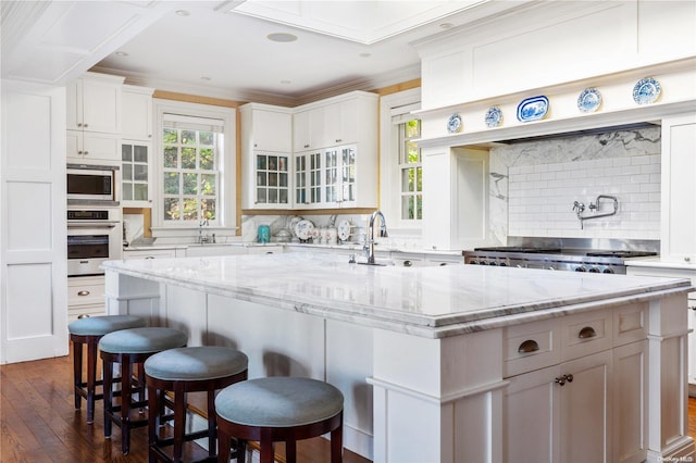 kitchen featuring appliances with stainless steel finishes, backsplash, a healthy amount of sunlight, and an island with sink