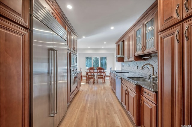 kitchen with backsplash, sink, built in appliances, dark stone countertops, and light hardwood / wood-style floors