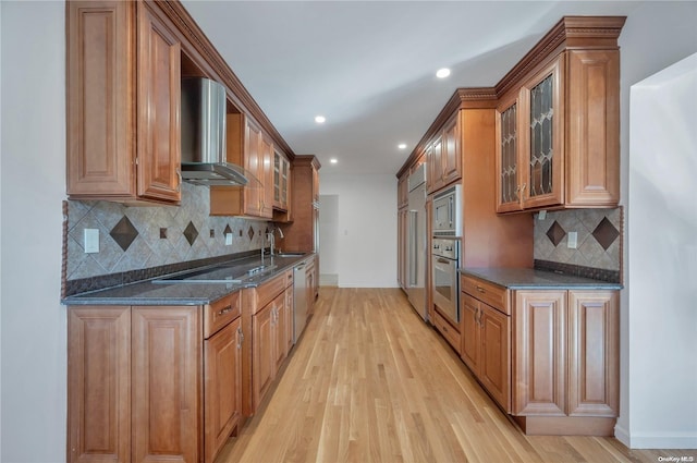 kitchen featuring backsplash, dark stone counters, wall chimney exhaust hood, light hardwood / wood-style floors, and stainless steel appliances