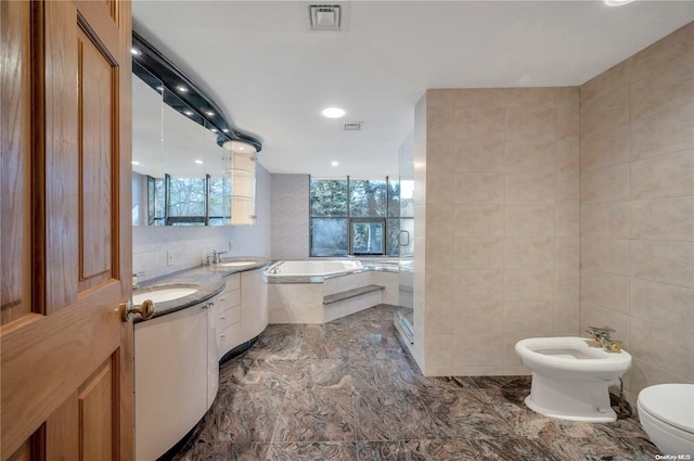 bathroom featuring vanity, a relaxing tiled tub, a bidet, tile walls, and toilet