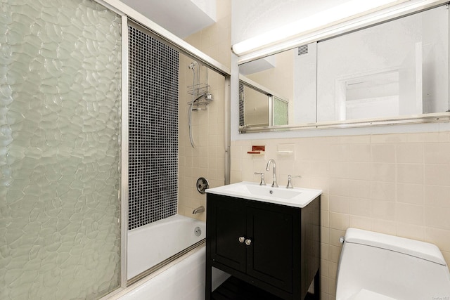 full bathroom with tile walls, vanity, bath / shower combo with glass door, and toilet