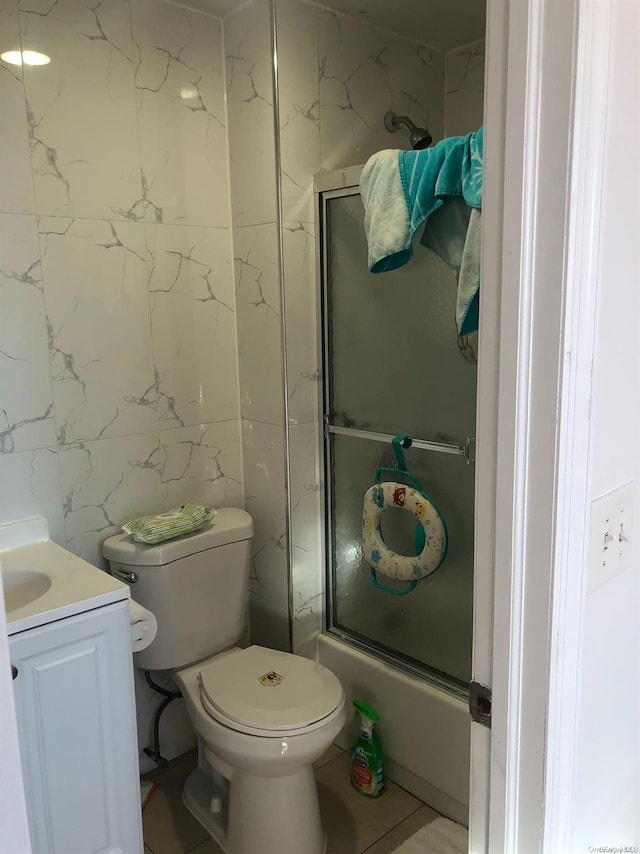 full bathroom with vanity, tile patterned floors, combined bath / shower with glass door, toilet, and tile walls