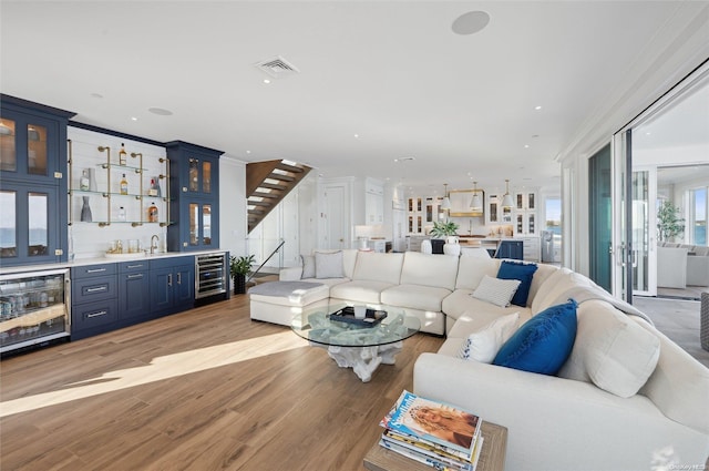 living room featuring crown molding, wet bar, light hardwood / wood-style floors, and wine cooler