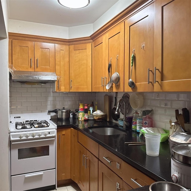 kitchen with backsplash, dark stone countertops, white gas range, and sink