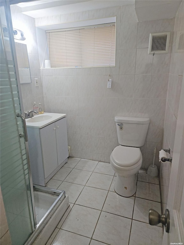 bathroom with tile patterned floors, vanity, tile walls, toilet, and a shower with shower door