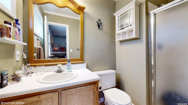 bathroom featuring a wealth of natural light, toilet, vanity, a shower with shower door, and ornamental molding