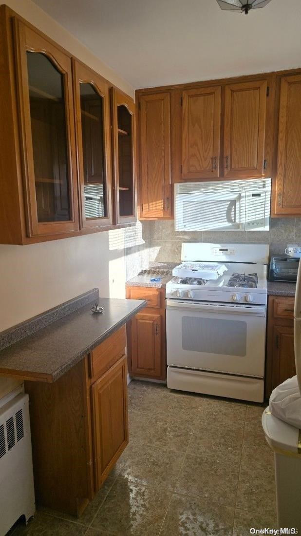 198-02 Pompeii Ave Unit 1B, Hollis, NY 11423 - kitchen featuring white appliances, radiator, decorative backsplash, brown cabinets, and glass insert cabinets