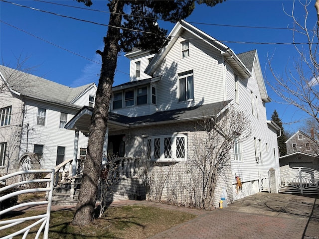 back of house with a shingled roof and decorative driveway