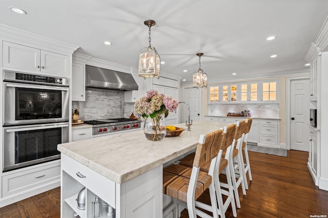 kitchen with a center island with sink, white cabinets, wall chimney range hood, appliances with stainless steel finishes, and dark hardwood / wood-style flooring