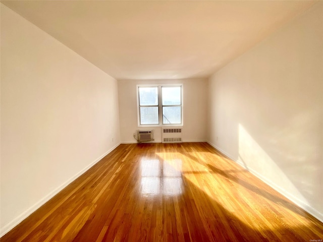 unfurnished room featuring a wall mounted air conditioner, radiator heating unit, and hardwood / wood-style flooring