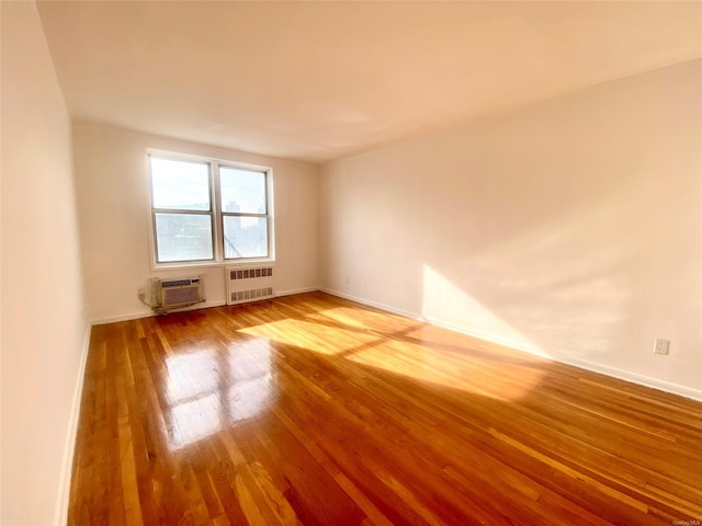 unfurnished room with an AC wall unit, radiator heating unit, and hardwood / wood-style flooring