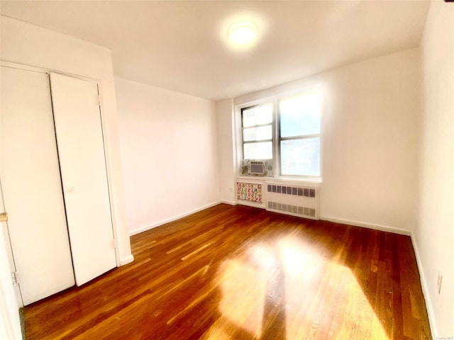 unfurnished bedroom with cooling unit, a closet, radiator, and wood-type flooring