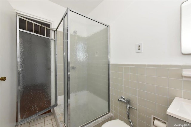 bathroom featuring tile patterned floors, vanity, a shower with shower door, and tile walls