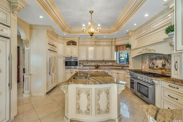 kitchen featuring sink, stainless steel appliances, an island with sink, pendant lighting, and cream cabinetry