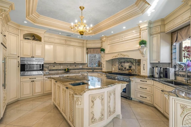 kitchen featuring a raised ceiling, sink, hanging light fixtures, an island with sink, and stainless steel appliances