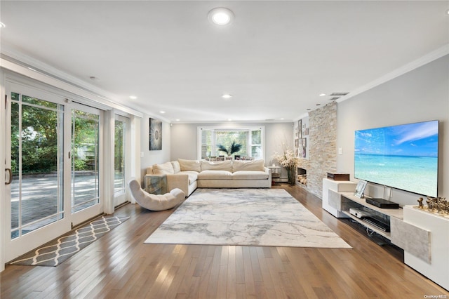 living room with a stone fireplace, hardwood / wood-style floors, and ornamental molding