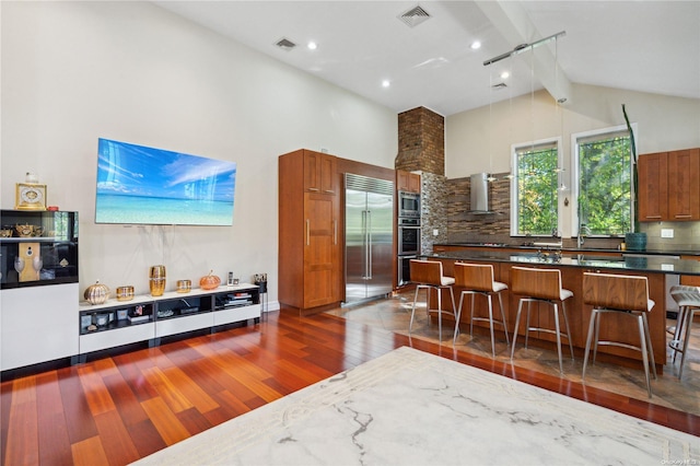 kitchen featuring a kitchen breakfast bar, tasteful backsplash, dark hardwood / wood-style flooring, high vaulted ceiling, and built in appliances