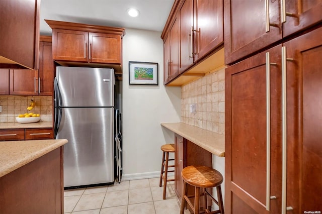 kitchen with light tile patterned flooring, backsplash, and stainless steel refrigerator