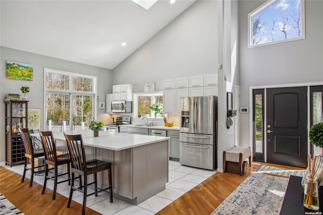 kitchen featuring a breakfast bar, a center island, high vaulted ceiling, appliances with stainless steel finishes, and light hardwood / wood-style floors