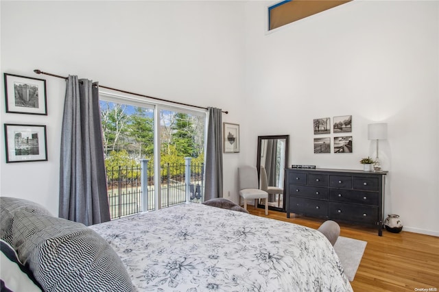 bedroom with access to exterior, wood-type flooring, and a high ceiling