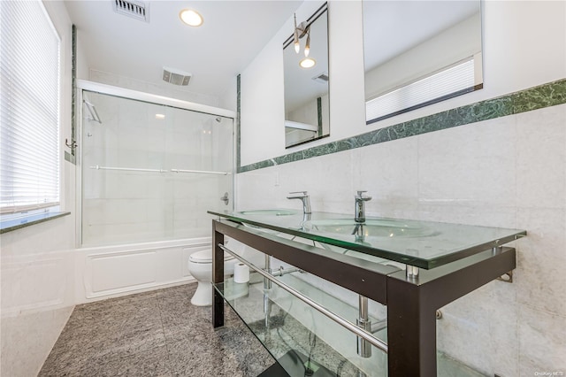 full bathroom featuring toilet, combined bath / shower with glass door, tile walls, and vanity