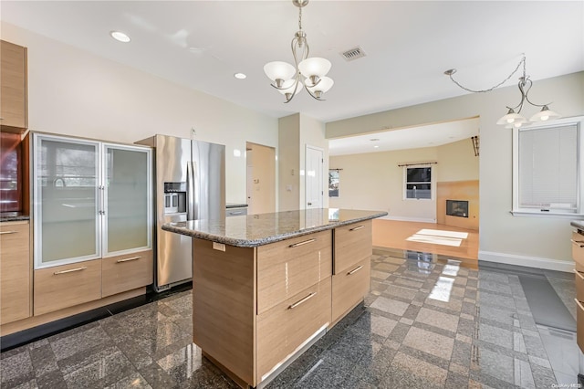 kitchen with stainless steel refrigerator with ice dispenser, dark stone counters, an inviting chandelier, a kitchen island, and hanging light fixtures