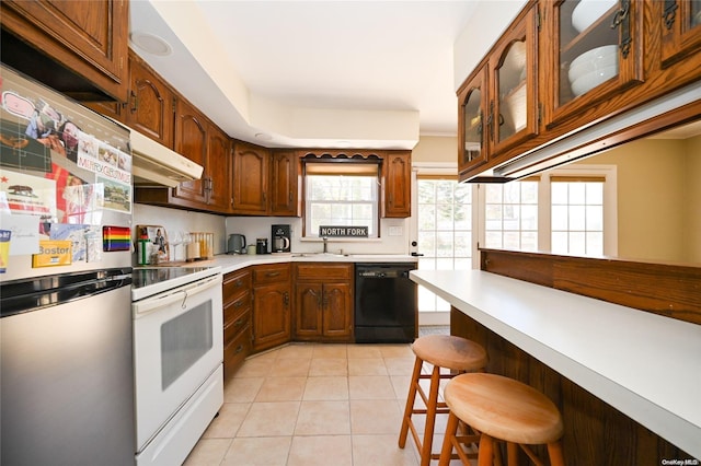 kitchen with dishwasher, white range with electric cooktop, light tile patterned floors, stainless steel refrigerator, and a breakfast bar