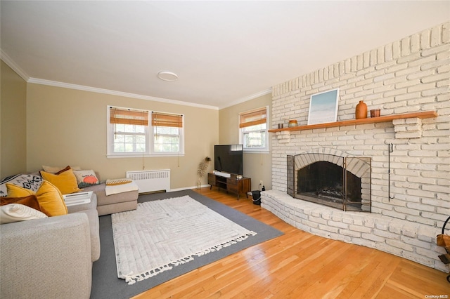 living room with hardwood / wood-style flooring, a brick fireplace, crown molding, and radiator heating unit