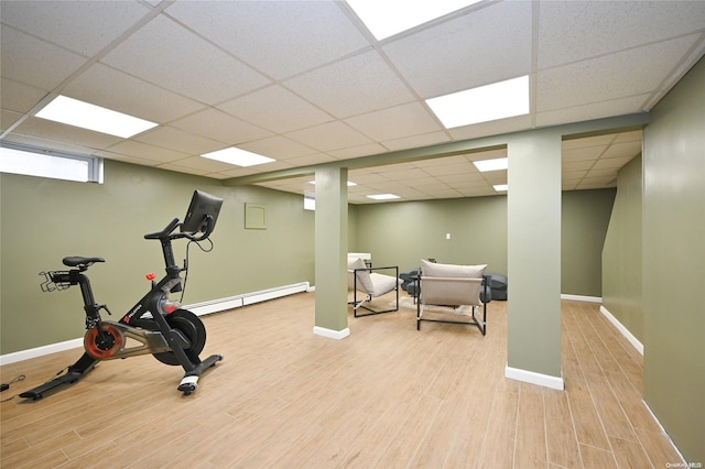 workout area with a paneled ceiling, baseboard heating, and light hardwood / wood-style flooring