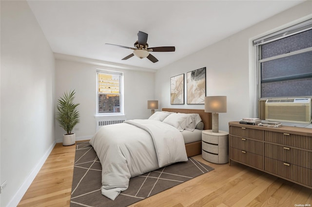 bedroom featuring ceiling fan, light hardwood / wood-style floors, radiator heating unit, and cooling unit