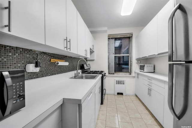 kitchen featuring appliances with stainless steel finishes, tasteful backsplash, sink, radiator heating unit, and white cabinetry