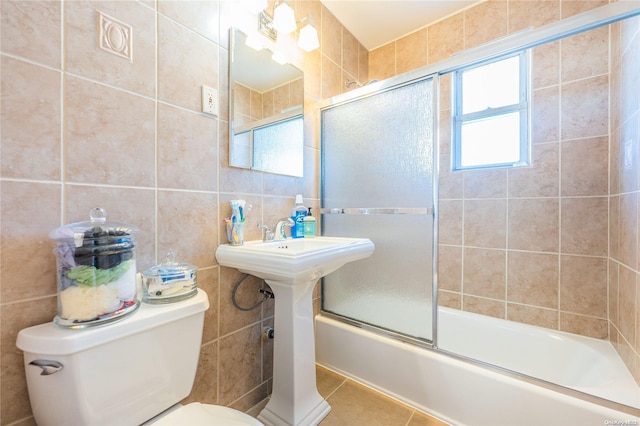 bathroom with tile patterned flooring, toilet, combined bath / shower with glass door, and tile walls