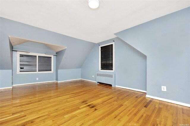 additional living space with radiator heating unit, light hardwood / wood-style floors, and vaulted ceiling