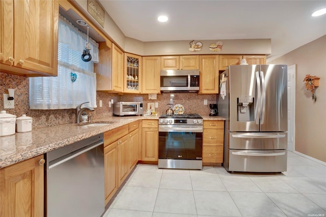 kitchen with backsplash, sink, appliances with stainless steel finishes, light tile patterned flooring, and light stone counters