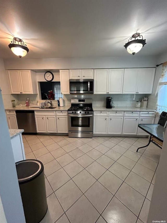 kitchen featuring backsplash, white cabinets, sink, light tile patterned floors, and appliances with stainless steel finishes