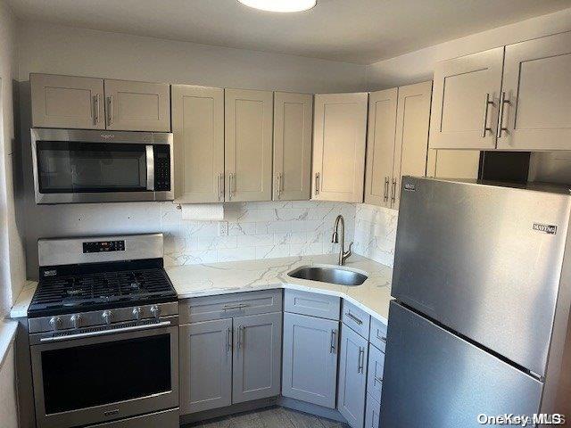 kitchen with backsplash, light stone countertops, sink, and appliances with stainless steel finishes