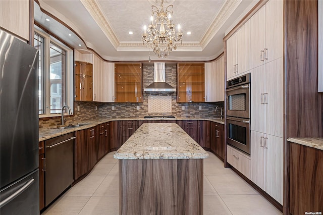 kitchen with wall chimney exhaust hood, stainless steel appliances, a raised ceiling, sink, and a center island