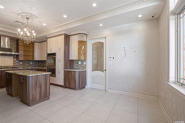 kitchen featuring wall chimney range hood, crown molding, pendant lighting, a kitchen island, and appliances with stainless steel finishes