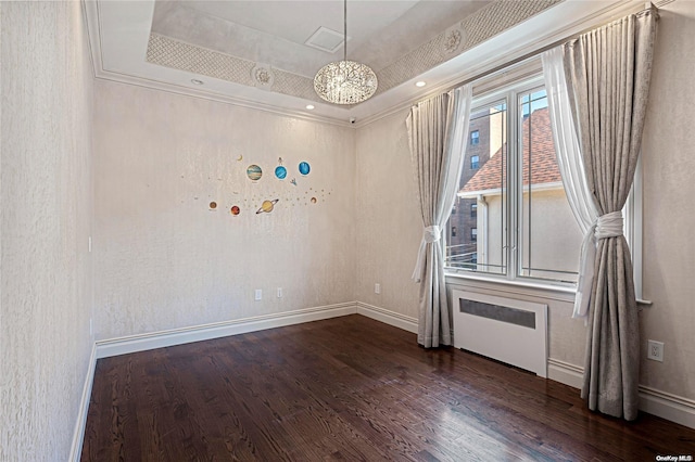 spare room featuring radiator heating unit, dark wood-type flooring, a raised ceiling, crown molding, and a chandelier