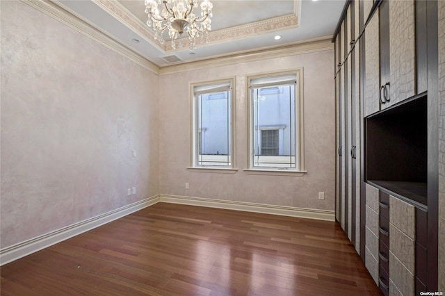 empty room featuring a tray ceiling, crown molding, dark hardwood / wood-style flooring, and a notable chandelier