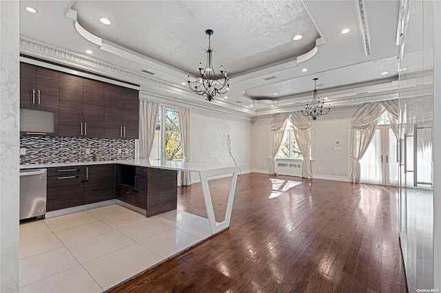 kitchen with decorative backsplash, dark brown cabinets, a tray ceiling, and stainless steel dishwasher