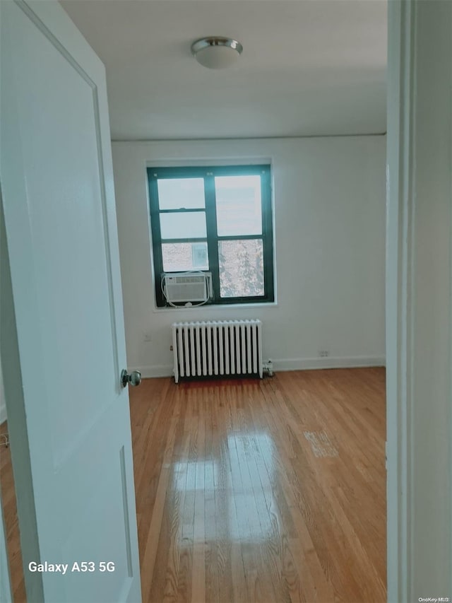 empty room with radiator heating unit, light wood-type flooring, and cooling unit