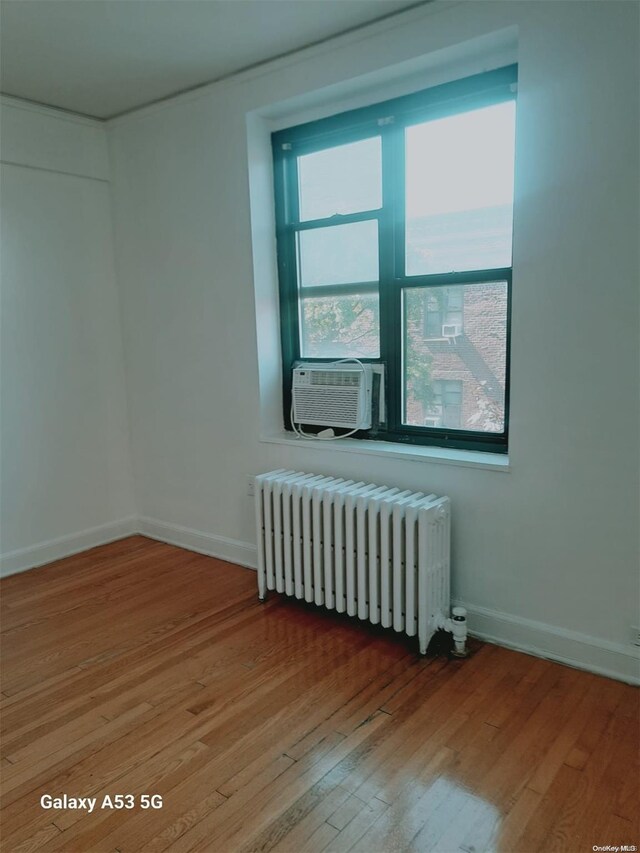 spare room featuring hardwood / wood-style flooring, cooling unit, and radiator