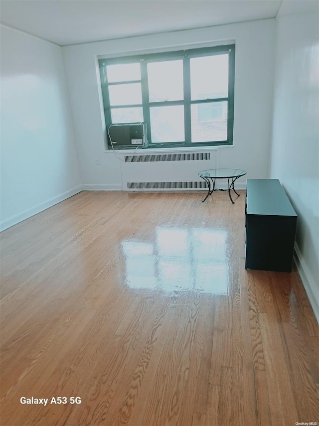 spare room featuring radiator heating unit, light hardwood / wood-style flooring, and cooling unit