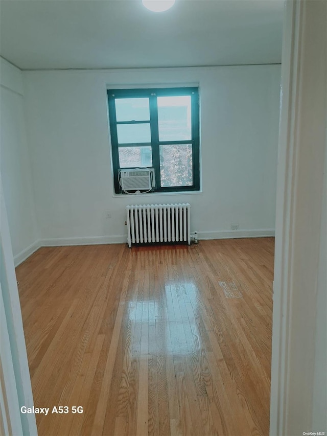 empty room featuring radiator heating unit, light hardwood / wood-style floors, and cooling unit