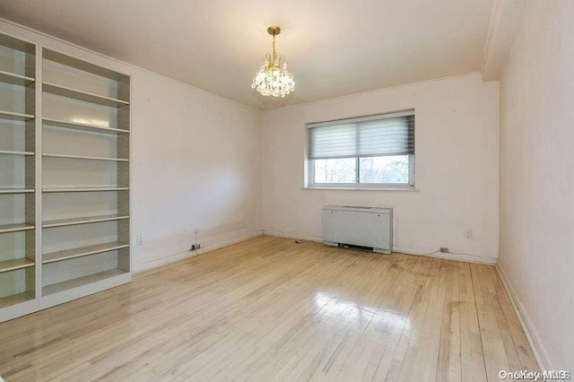 empty room featuring a chandelier, radiator heating unit, and hardwood / wood-style flooring