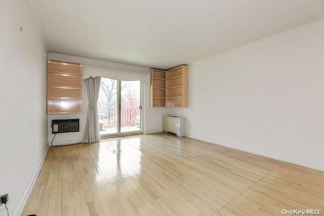 unfurnished living room with a wall mounted air conditioner, light hardwood / wood-style floors, and radiator