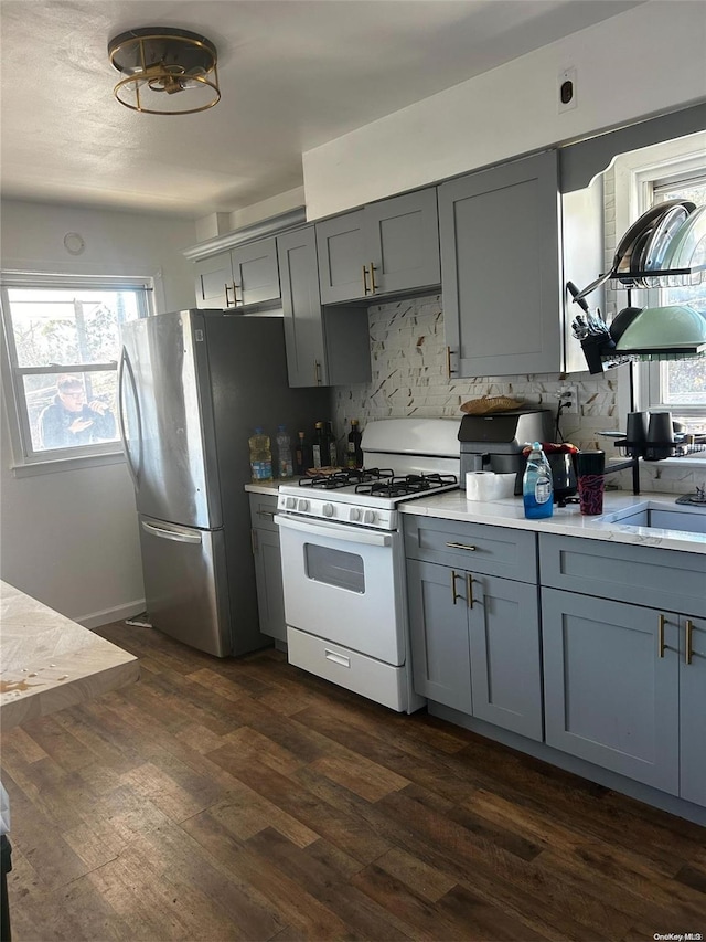 kitchen featuring backsplash, dark wood-type flooring, stainless steel fridge, gray cabinets, and white range with gas cooktop