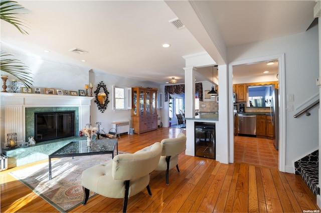 living room with wine cooler, light hardwood / wood-style floors, ornamental molding, and radiator